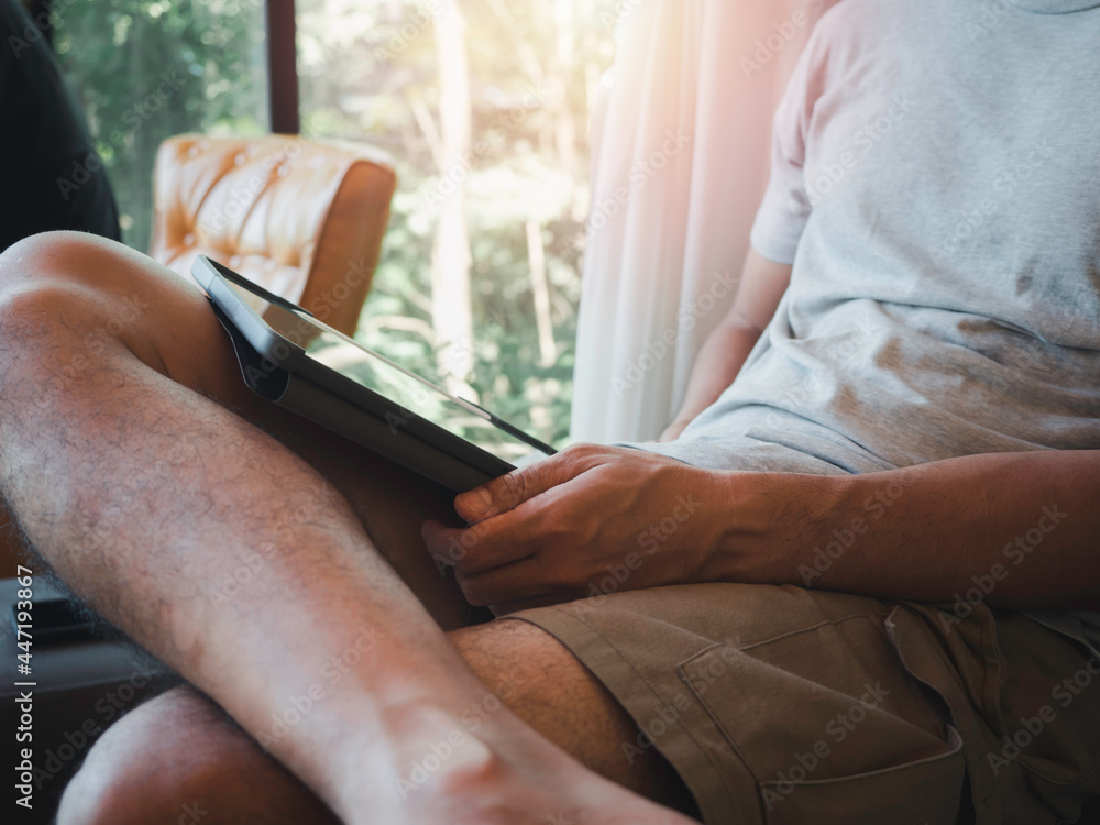 Hand man using digital tablet. A young person, man in casual grey shirt and shorts sitting and interacting with technology at home. Relaxation businessman working online at anywhere concept.