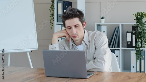Tired sleepy overworked exhausted caucasian man freelancer feels overwhelmed stress suffers from drowsiness falling asleep at workplace sitting at table with laptop falls under desk on floor in office photo