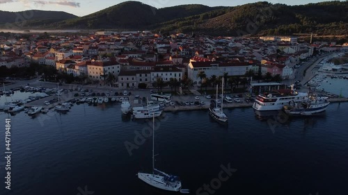 Early morning drone flight over quiet harbour with cars flying diagonally over houses on croatian island