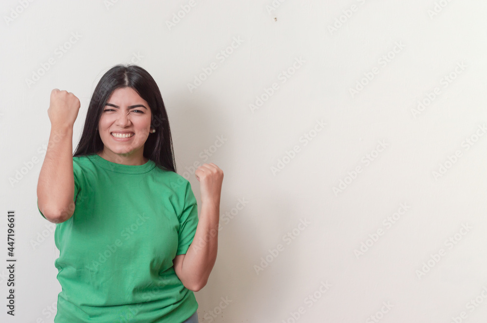young white latin girl with black hair and dressed in green making a winning expression with her hands on a white background young white latin girl with black hair and dressed in green making a winning expression with her hands on a white background