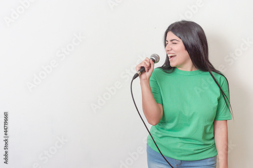 young white latin girl with black hair dressed in green with a microphone singing over a white background