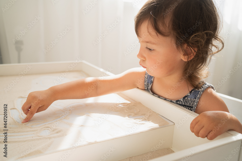 Sand drawing table for children. A little girl draws with her finger on