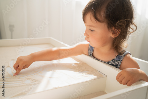 Sand drawing table for children. A little girl draws with her finger on a light sand table. Creative development in young children.