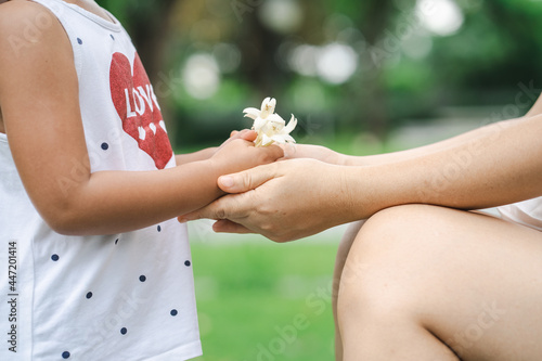 Small girl giving her mother white bouquet flowers at park. 