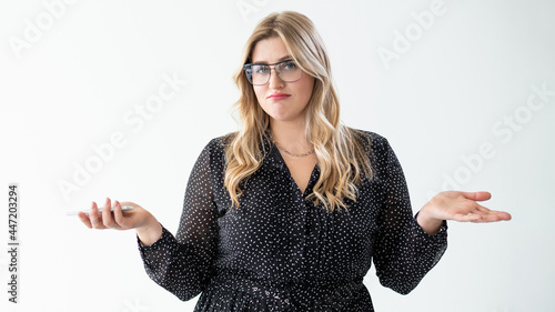 Confused woman portrait. Clueless shrug. Body positive. Whatever gesture. Indifferent disappointed overweight obese model comparing invisible options no idea sorry isolated on white. photo