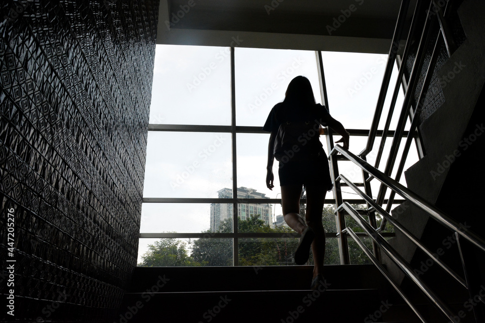 Fototapeta premium The young woman was stepping up the stairs of a tall building. silhouette