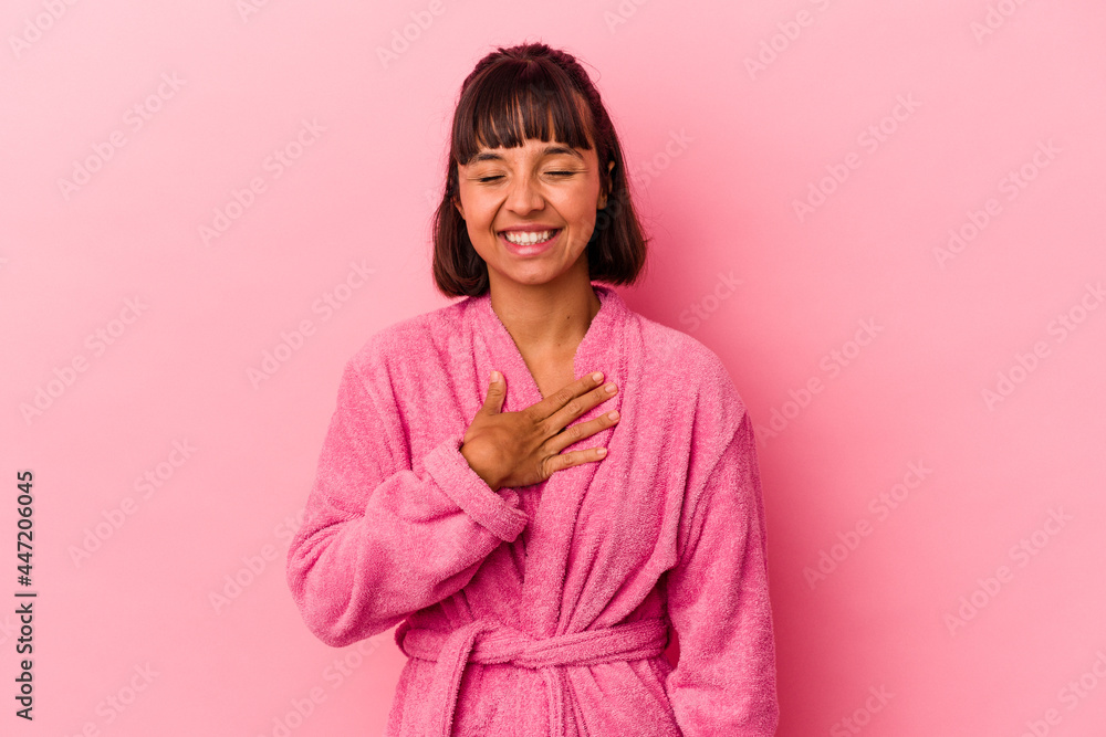 Young mixed race woman wearing a bathrobe isolated on pink background laughs out loudly keeping hand on chest. Young mixed race woman wearing a bathrobe isolated on pink background laughs out loudly keeping hand on chest.