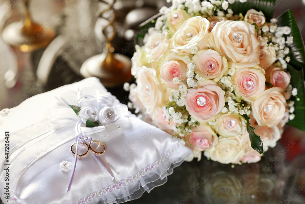 Two gold wedding rings displayed on cushion with bridal bouquet Two gold wedding rings displayed on cushion with bridal bouquet