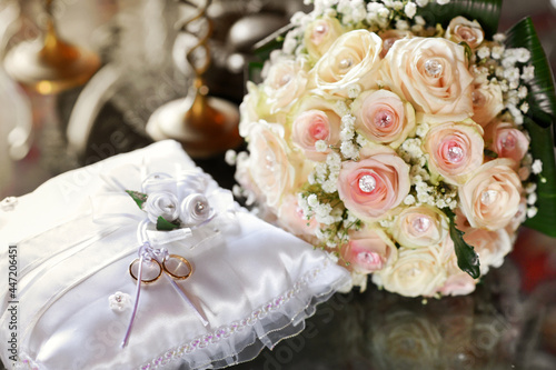 Two gold wedding rings displayed on cushion with bridal bouquet