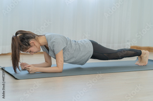 Fit, Sporty person asian young beautiful woman, girl doing yoga pose planking and physical, training and practice strong on mat in living room. Workout fitness exercise people in casual wear at home.