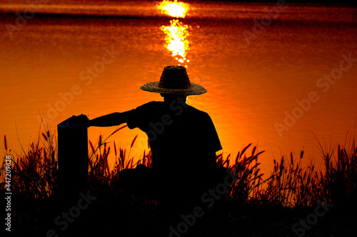 A silhouette of a farmer wearing a hat waiting for hope in the golden rays of the sun.