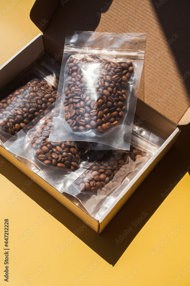 Roasted arabica sample coffee box with beans in blank transparent plastic bag with zipper on yellow background. Specialty and alternative trendy photo with shadow concept. Mock up, top view Roasted arabica sample coffee box with beans in blank transparent plastic bag with zipper on yellow background. Specialty and alternative trendy photo with shadow concept. Mock up, top view