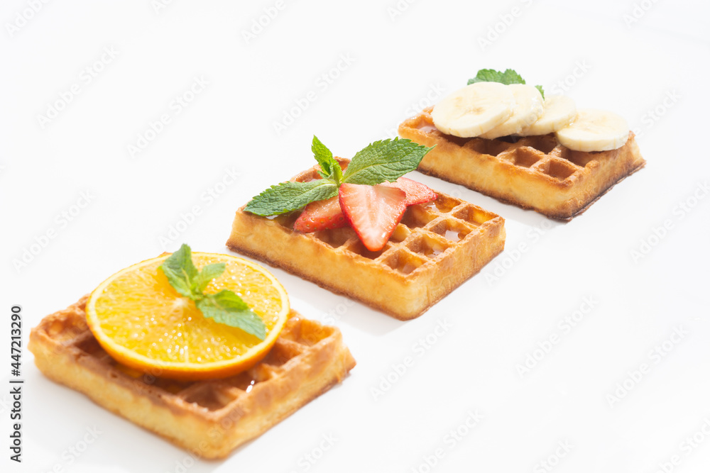 Belgium waffles with strawberry, banana and orange with syrup on white Belgium waffles with strawberry, banana and orange with syrup on white