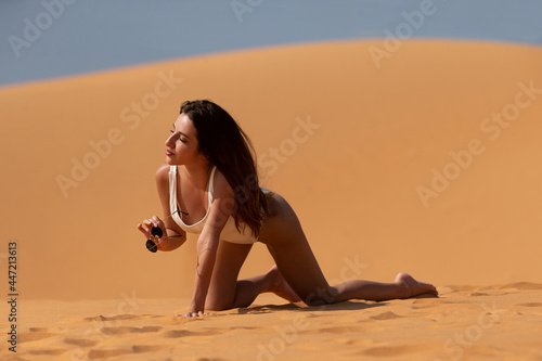 Close up side view of a tan sexy woman in a white swimsuit lying on sand relaxing on beach.