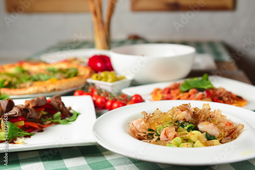 Shrimp pasta, carpaccio salad, spinach pizza, green olives and cherry tomatoes on the table. Italian concept, side view.