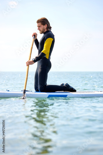 Paddle board sportsman standing paddling away on stand up paddleboarding at sea. Strong athlete male is standing on sup surfboard, watersport leisure activity, extreme sport concept