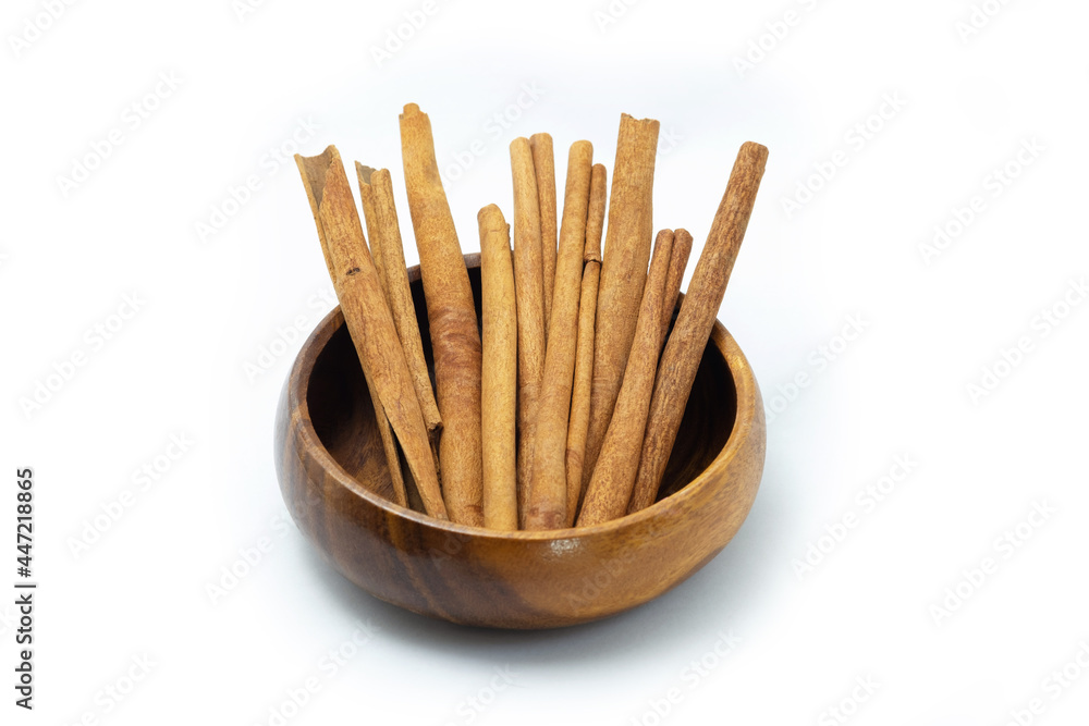Cinnamon sticks in wooden bowl on white background.
