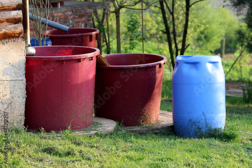 Various size shape and colors plastic barrels used for storing rainwater from gutter pipes on suburban family house corner to be used as part of garden drip irrigation system at urban garden on warm