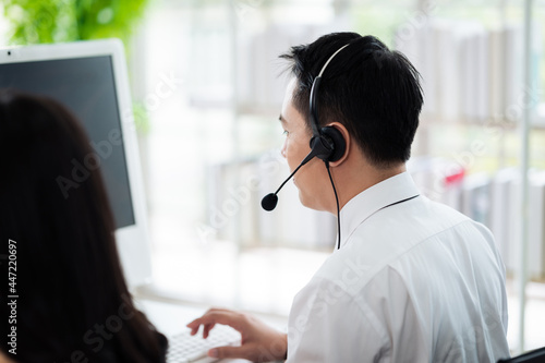 Team of call center staff in Asia wears headphones with a microphone. Smile while serving customers at desks and computers. Service concept and consulting. Communication concept.
