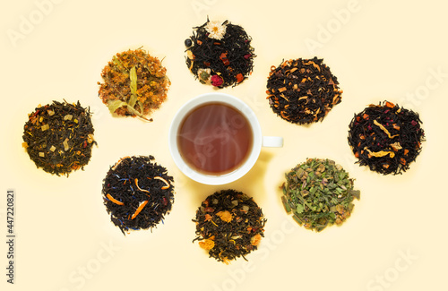 Cup of tea on yellow table with large assortment of herbal, flower, berry and leaf dry teas.