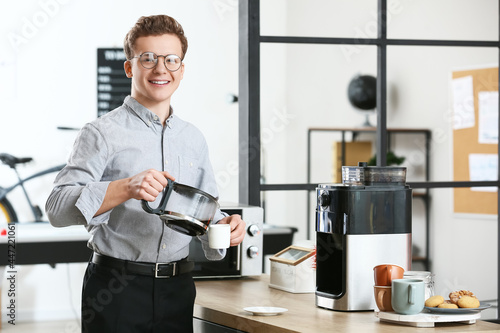 Young man pouring coffee into cup in office