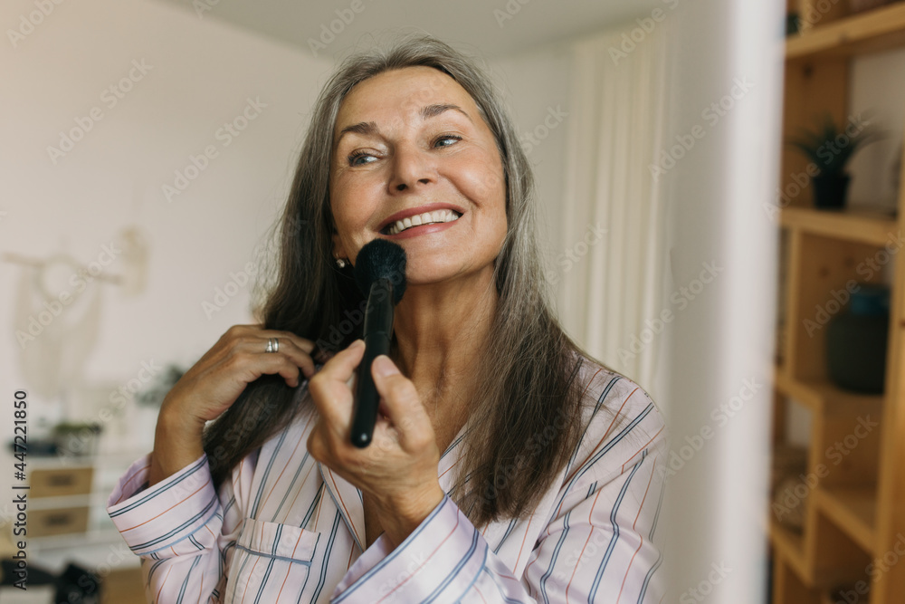 Cheerful senior woman applying cosmetics product with professional brush at home. Natural makeup for aging skin. Take care of yourself, wellness and beauty rituals concept Cheerful senior woman applying cosmetics product with professional brush at home. Natural makeup for aging skin. Take care of yourself, wellness and beauty rituals concept