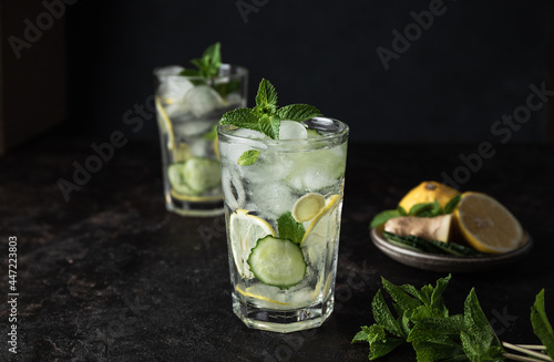 Detox Sassy Water. Cool and fresh drink with lemon, cucumber, mint, ginger and ice. Two glasses of lemonade on a black background. Copy space
