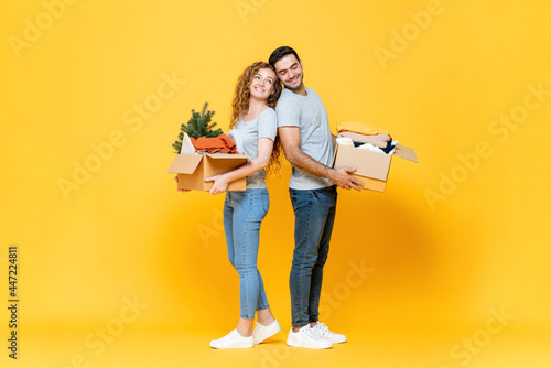 Happy interracial couple carrying stuff in yellow studio isolated background, moving house concept