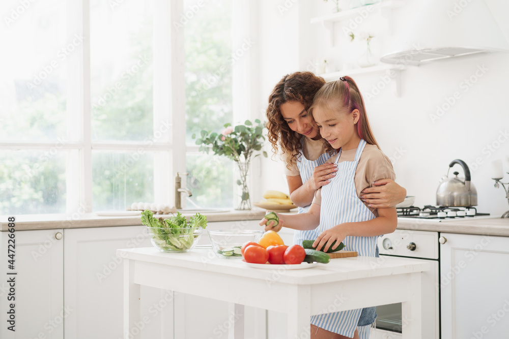 Mother and teen daughter preparing vegetable salad at kitchen