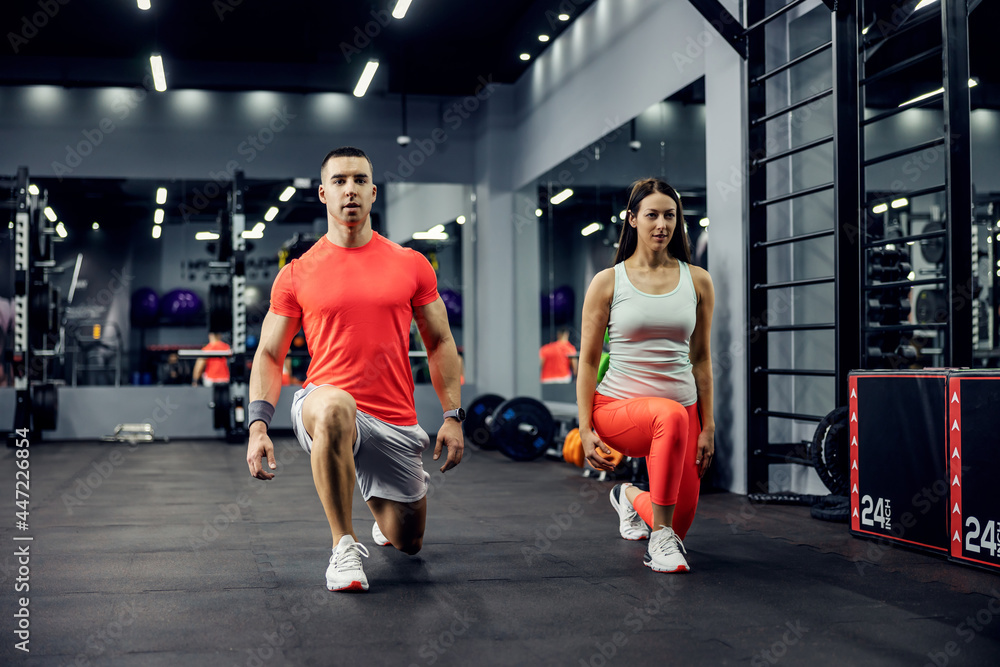 Obraz premium A cute sports couple exercising steps forward for legs and buttocks on a black floor in an indoor gym with a mirror. Fitness and sports lifestyle