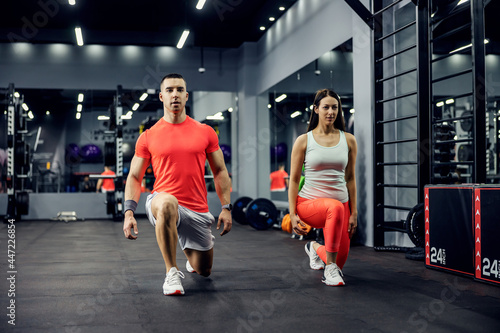 A cute sports couple exercising steps forward for legs and buttocks on a black floor in an indoor gym with a mirror. Fitness and sports lifestyle