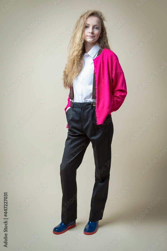 Full Length Portrait of Caucasian Teenager in School Uniform With Suspenders And Pink Jumper With Wellington Ruber Boots Over Beige. Full Length Portrait of Caucasian Teenager in School Uniform With Suspenders And Pink Jumper With Wellington Ruber Boots Over Beige.