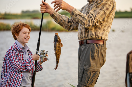 Catch of the day. Child boy engaged in fishing hobbies With grandfather. copy space. happy redhead kid boy enjoy fishing at summer, holds fishing rod with caught fish. focus on fish