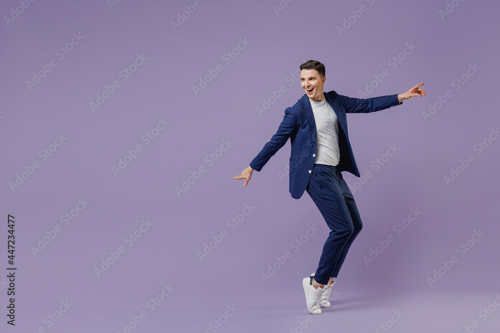 Full size young successful employee business man lawyer 20s wear formal blue suit white t-shirt work in office stand on toes have fun spread hands isolated on pastel purple background studio portrait. Full size young successful employee business man lawyer 20s wear formal blue suit white t-shirt work in office stand on toes have fun spread hands isolated on pastel purple background studio portrait.