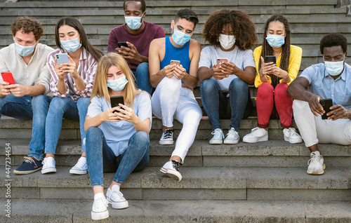 Young multiracial group of friends using mobile smartphone while wearing face mask during covid19 - Youth millennial lifestyle concept