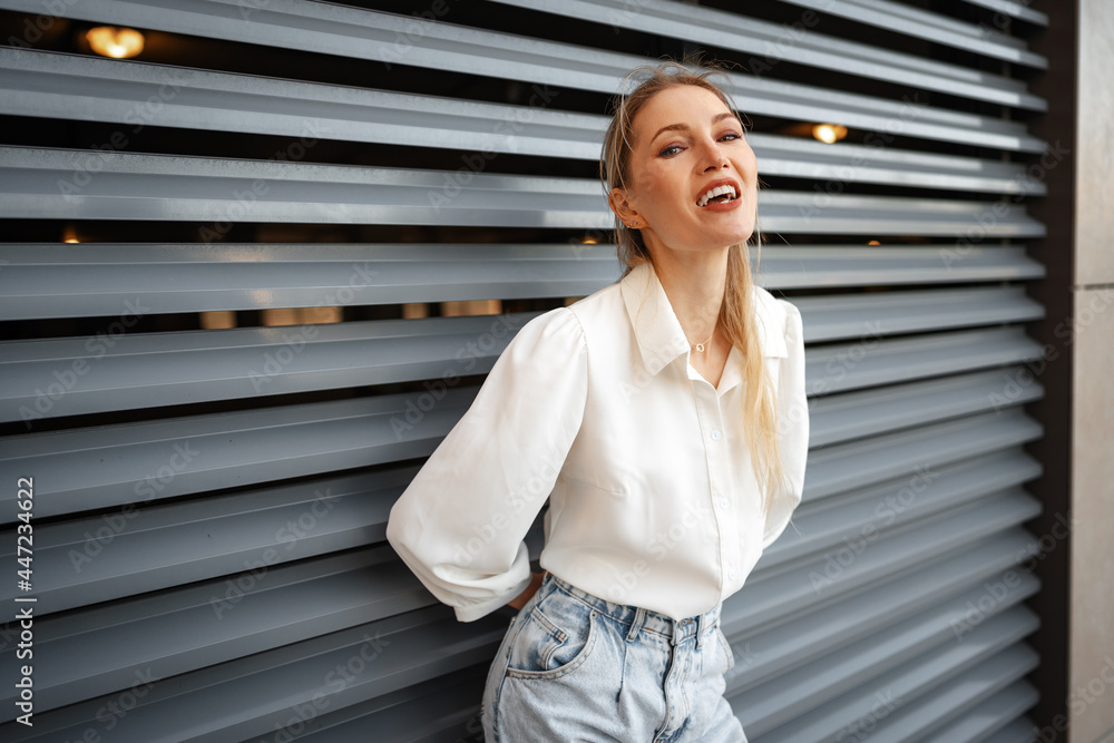 Stylish girl in jeans and white cotton blouse posing near gray wall Stylish girl in jeans and white cotton blouse posing near gray wall