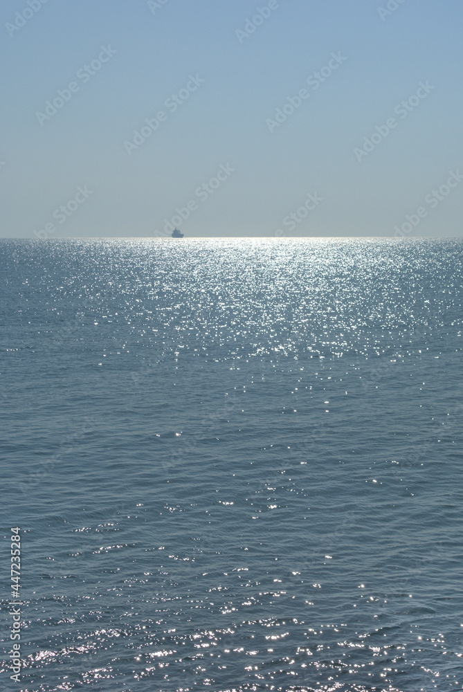 Calm sea, clear sky and morning sun with a ship on the horizon