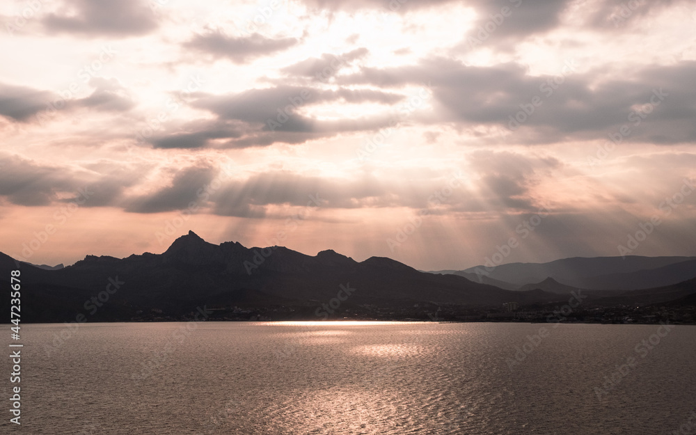 Photography of the sunset on the lake. Orange reflection on the water, mountains in the background. Dramatic view, breathtaking seascape. Golden sun rays.