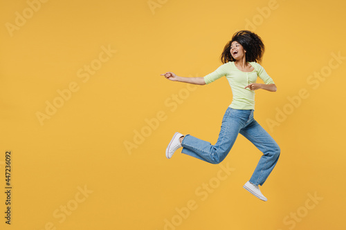 Full size body length smiling overjoyed african american young woman 20s wears green shirt jump pointing back on workspace area copy space mock up closed isolated on yellow background studio portrait