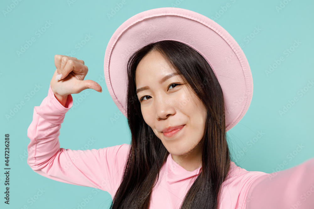 Close up young brunette asian woman 20s wears pink clothes wide brim hat doing selfie shot on mobile cell phone point thumb finger on herself isolated on pastel blue color background studio portrait Close up young brunette asian woman 20s wears pink clothes wide brim hat doing selfie shot on mobile cell phone point thumb finger on herself isolated on pastel blue color background studio portrait