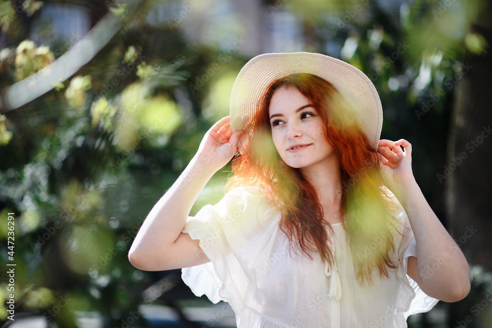 Portrait of young woman with hat standing outdoors in city in summer.