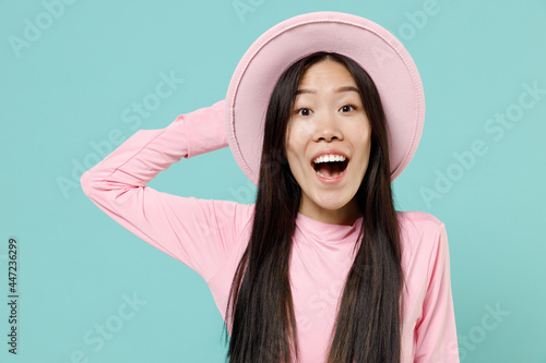 Cute charismatic fascinating stunning fun young brunette asian woman 20s wear pink clothes hat look camera isolated on pastel blue color background studio portrait. People emotions lifestyle concept.