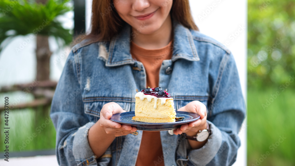 Closeup image of a young asian woman holding and showing a plate of blueberry cheesecake Closeup image of a young asian woman holding and showing a plate of blueberry cheesecake