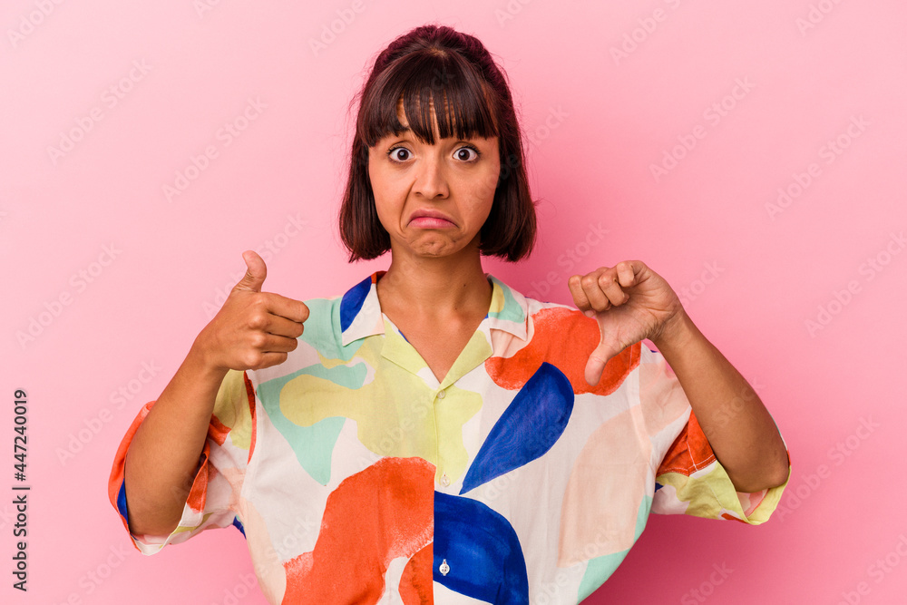 Young mixed race woman isolated on pink background showing thumbs up and thumbs down, difficult choose concept