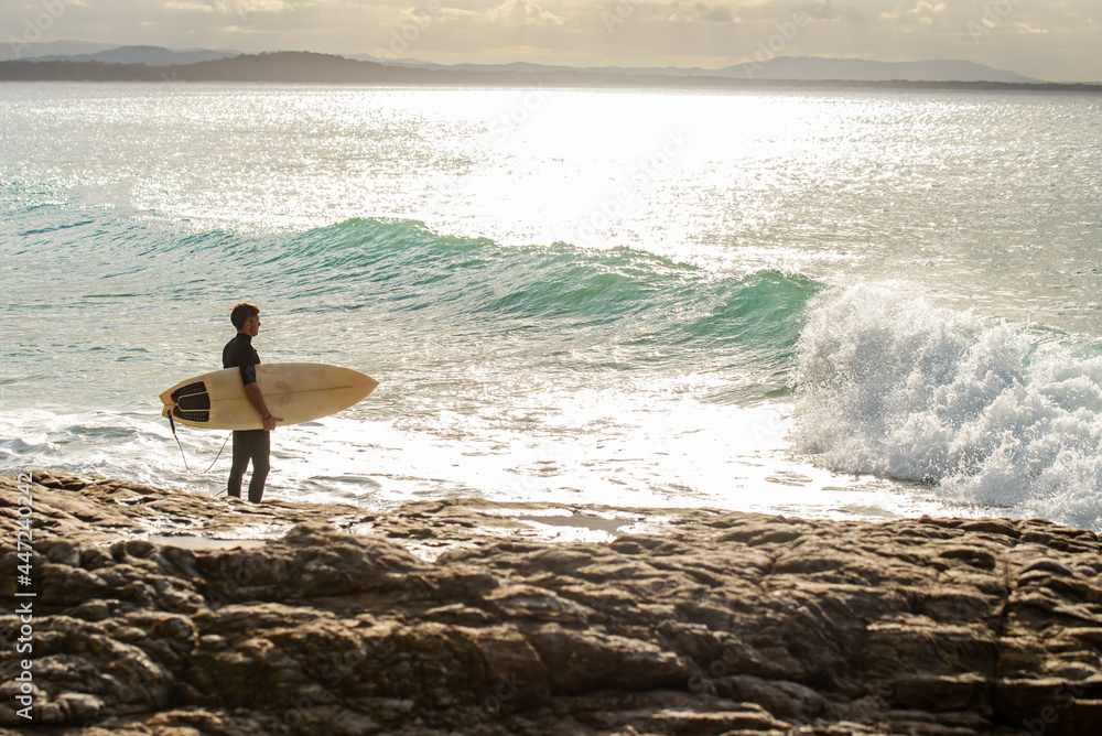 Young Surfer Standing on Rocks Watching the Waves in a Sunny Day. Copy Space Young Surfer Standing on Rocks Watching the Waves in a Sunny Day. Copy Space