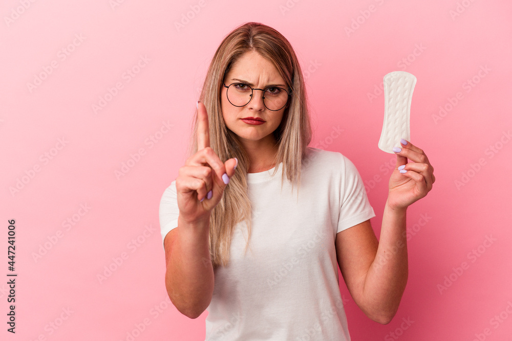 Young russian woman holding a compress isolated on pink background showing number one with finger. Young russian woman holding a compress isolated on pink background showing number one with finger.
