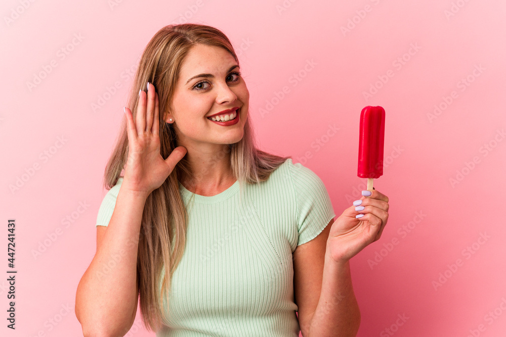 Young russian woman holding an ice cream isolated on pink background trying to listening a gossip. Young russian woman holding an ice cream isolated on pink background trying to listening a gossip.