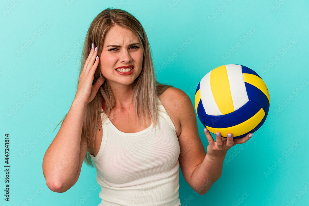 Young russian woman playing volleyball isolated on blue background covering ears with hands.