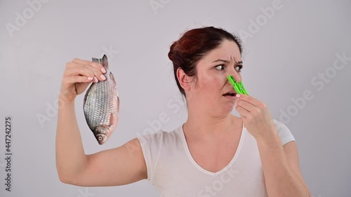 Caucasian woman is horrified by the smell of fish and pinches her nose with a clothespin on a white background. photo