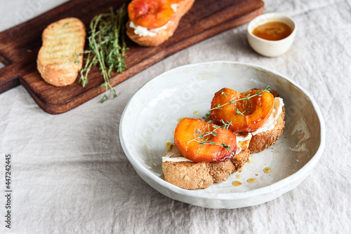 Summer Breakfast - toast (sandwich, bruschetta) with grilled peaches, cream cheese (ricotta, mascarpone), thyme and honey on beige linen tablecloth. Selective focus